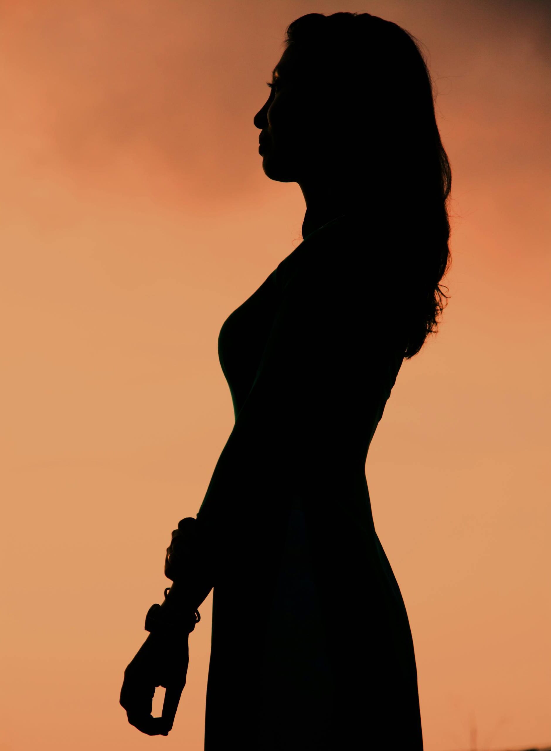 A striking silhouette of a woman against an orange sunset sky, creating a serene and dramatic mood.